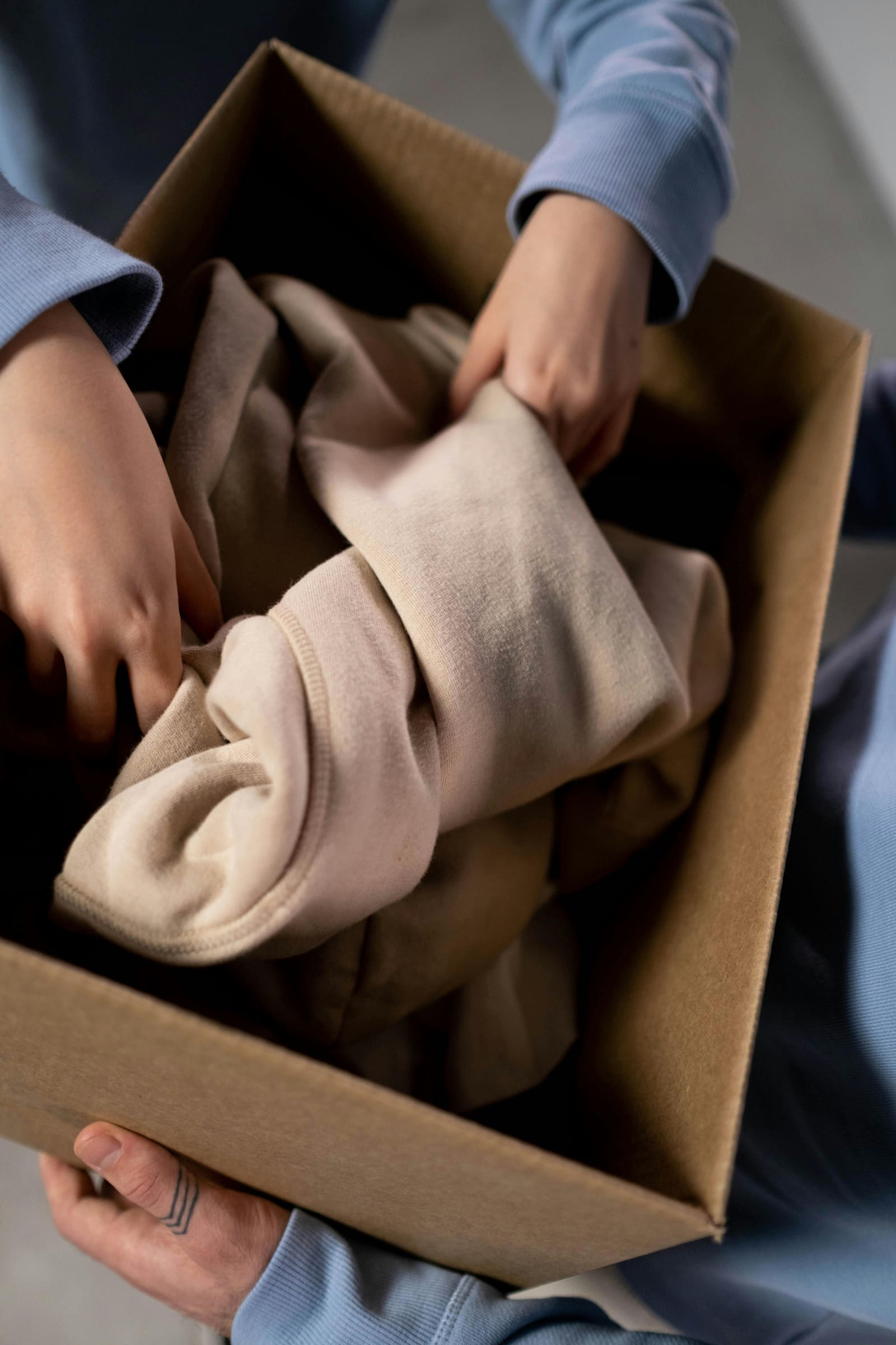 Hands folding clothing into a cardboard box, ready for donation pickup.