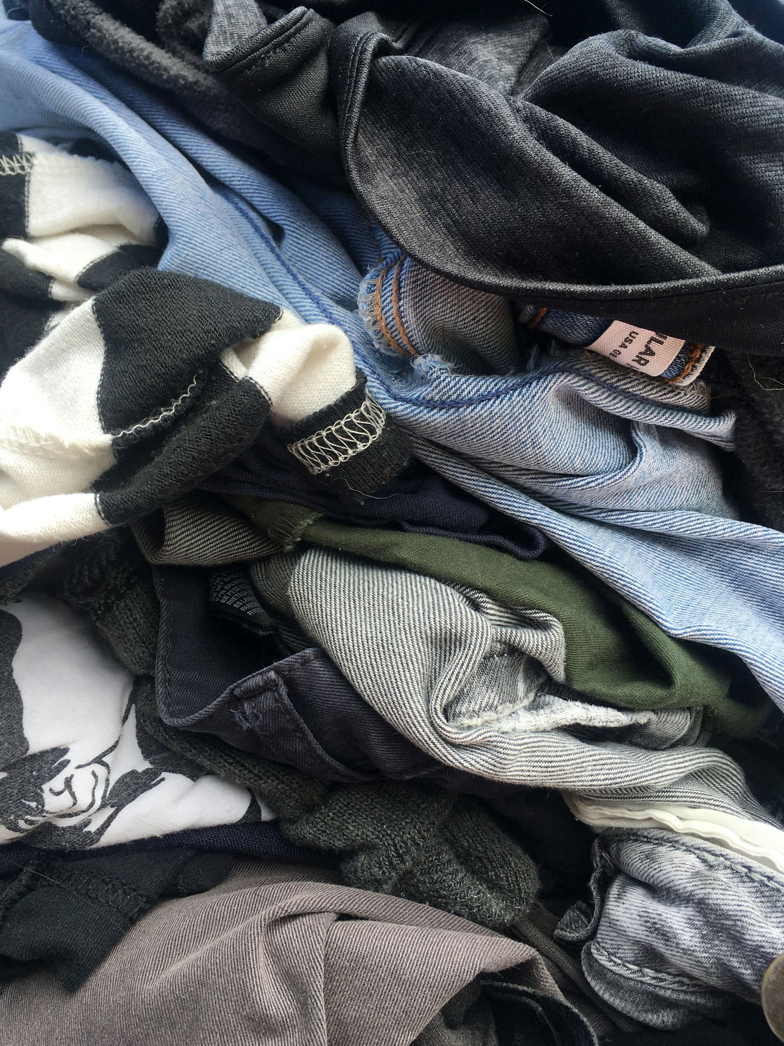 Mixed denim and tee pile, sunlit warm tones.